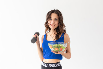 Healthy lifestyle, people and sport concept - Healthy young woman with vegetables and dumbbells promoting a healthy fitness and eating lifestyle