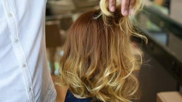 Hairdresser gives final touch to beautiful red hair of Caucasian young woman