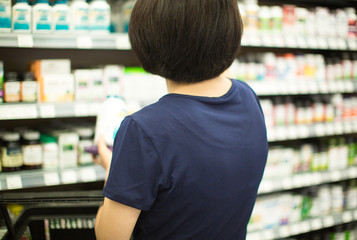 Woman Shopping at Grocery Market Pharmacy. Supermarket Shopper Doing Groceries. Female Holding Basket Trying to Decide which Products to Buy. Retail Healthcare Medicine, Vitamins, and Supplements.