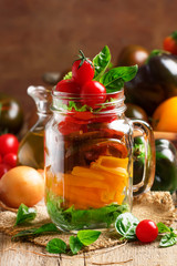 Vegan salad jar with yellow, black and red cherry tomatoes with bell peppers, onions, lettuce, basil and olive oil. Trendy food,  vintage wooden kitchen table background, selective focus