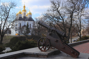 Fototapeta na wymiar The historical center of the ancient Ukrainian city of Chernigov. Old cannon on the rampart. Beautiful white church with golden domes. Travel to historical sites photo