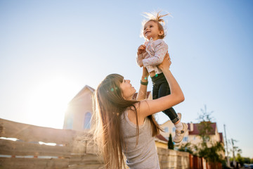 Mother lift up her little daughter. New house on background.