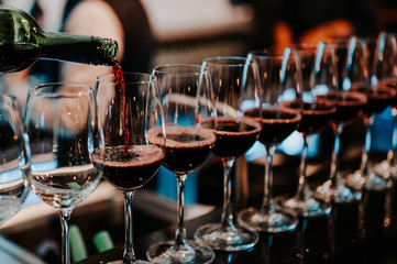 Bartender pours red wine in glasses at bar.Male sommelier pouring red wine into long-stemmed wineglasses.