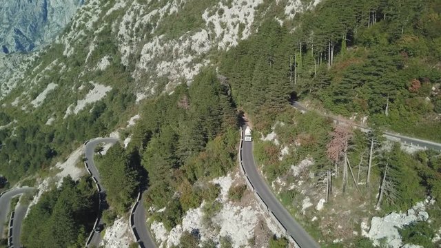 The serpentines road on the side of the mountain cliff with the aerial view of the high mountains. Stock. Aerial View landscape serpentine road winding on the mountains background in summer sunny day