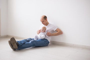 Infant baby, family and fatherhood concept - happy bald father holding baby daughter on knees on white background
