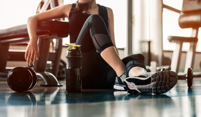 Fitness woman Relaxing after exercise with a whey protein and dumbbell placed beside the...