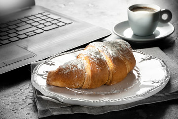 Morning in office. Coffee and fresh croissant for breakfast near notebook. Dark table in grange style.