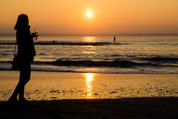 Fototapeta premium Silhouette of a young girl with a glass of aperol spritz with man on paddle surf on background at sunset on North Sea 