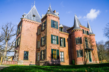 Netherlandish Castle Keukenhof with green shutters from low angle with green lawn on foreground and blue sky with a few clouds 