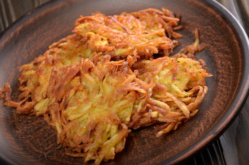 Fresh homemade tasty potato pancakes in clay dish on rustic wooden table