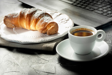 Breakfast of businessman. Coffee and croissant for breakfast next to notebook. Office style.