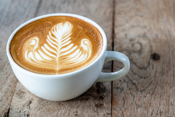 Close up caffe latte art coffee with flat milk in white ceramic coffee cup on wooden table in coffee shop cafe restaurant with morning sunlight. Concept for coffee lover or relaxation mood.