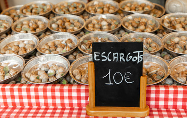 Display of snails (escargots) for sale with price sign in Parisian outdoor market with red and white checked tablecloth