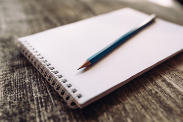 A pencil and a notebook on wooden surface close up.