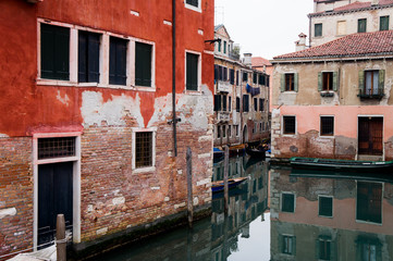 Fototapeta na wymiar Venice canal street with houses reflecting in water with red old walls and windows 