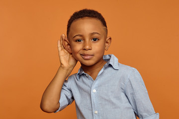 Overhear, spy and secrecy concept. Isolated studio portrait of cute nosy African ten year old boy...