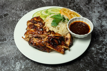 a plate of chicken rice with soup and sauce on dark background.