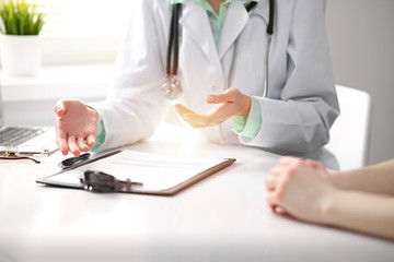 Doctor and  female patient sitting at the desk and talking  in clinic near window. Medicine and health care concept. Green is main color