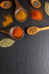 Different aromatic spices in wooden spoons on dark grey background