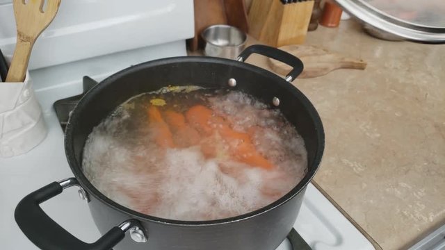 Home cooking - Carrots being intensively boiled in non stick pot while lifting glass lid and exposing vegetables inside.