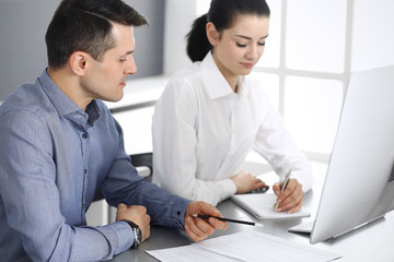 Cheerful smiling businessman and woman working with computer in modern office. Headshot at meeting or workplace. Teamwork, partnership and business concept 
