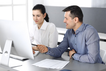 Cheerful smiling businessman and woman working with computer in modern office. Headshot at meeting or workplace. Teamwork, partnership and business concept 