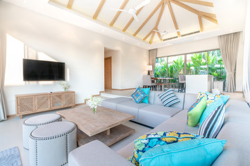 Luxury interior design in living room of pool villas. Airy and bright space with high raised ceiling, sofa, middle table, dining table and open kitchen home