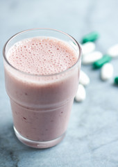Glass of Protein Shake with milk and raspberries. BCAA amino acids and L - Carnitine capsules in background. Sport nutrition. Bright tone background. Close up. Copy space. 