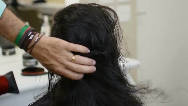 Hairdresser drying long black hair of young girl in beauty saloon