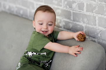 Naklejka premium The one-year-old boy is sitting on a gray sofa with a walnut and smiled happily. Positive lifestyle concept. Happy childhood.