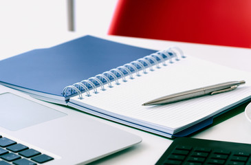 Closeup of white desktop with laptop, coffee cup, notepads, pen, calculator and other items.