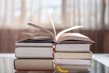 Open book on a stack of books on a table in a bright room. Education and reading of paper books