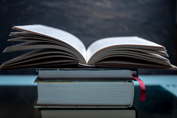 Open book on a stack of books on a table on a dark background. Exam preparation in schools and colleges