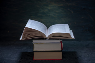 Open book on a stack of books on a table on a dark background. Exam preparation in schools and colleges