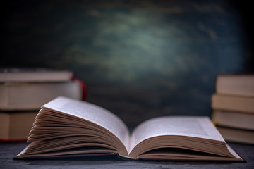 Open book on a stack of books on a table on a dark background. Education and reading of paper books