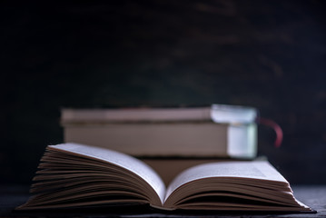 Open book on a stack of books on a table on a dark background. Education and reading of paper books