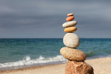 Rock zen pyramid of colorful pebbles on a sandy beach on the background of the sea. Concept of balance, harmony and meditation.