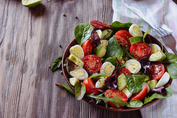 Delicious salad with cherry tomatoes, avocado, herbs, quail egg  pieces in a salad bowl on a wooden table
