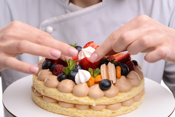 Girl cook a cake decorated with berries, strawberries, raspberries and mint