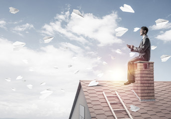 Man on brick roof reading book and paper planes flying in air