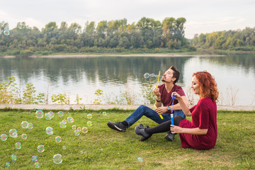 Family, people concept - young couple blowing soap bubbles near the river