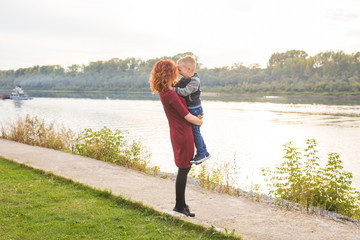 Motherhood and children concept - young mother with son in her arms near the river