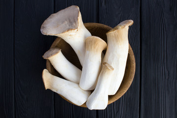 Mushrooms eringi in the brown bowl  on the black wooden background.Top view.Closeup.