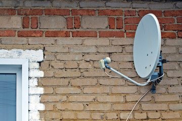 Satellite dish close-up on a wall of white brick.