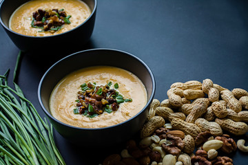 Pumpkin cream soup with herbs and nuts, served in a dark bowl. Proper and healthy food. Vegetarian dish. Dark background.