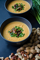 Pumpkin cream soup with herbs and nuts, served in a dark bowl. Proper and healthy food. Vegetarian dish. Dark background.