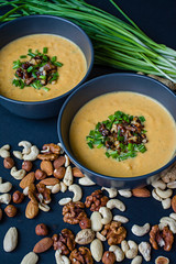 Pumpkin cream soup with herbs and nuts, served in a dark bowl. Proper and healthy food. Vegetarian dish. Dark background.