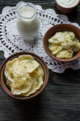 Dumplings with potatoes and cabbage. Sour cream, milk and greens. Traditional dish of Ukraine. Dark wooden background.