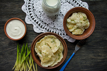 Dumplings with potatoes and cabbage. Sour cream, milk and greens. Traditional dish of Ukraine. Dark wooden background.