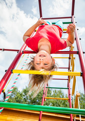 Little girl hanging from a jungle gym playing in a summer garden - child risky play concept